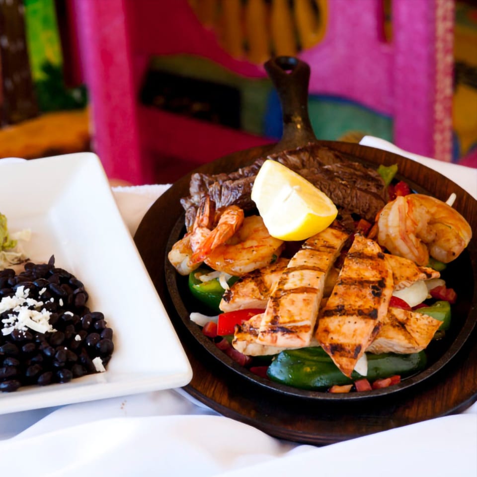 Sizzling El Coronel fajitas with grilled chicken, steak, shrimp, peppers, onions, and black beans.