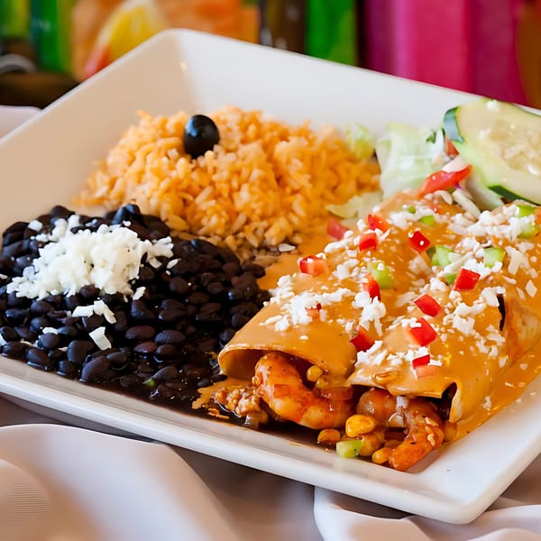 Shrimp enchiladas with creamy sauce, rice, black beans, and a side salad on a white plate.