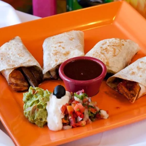 Four burritos with guacamole, sour cream, pico de gallo, and a side of dark sauce.