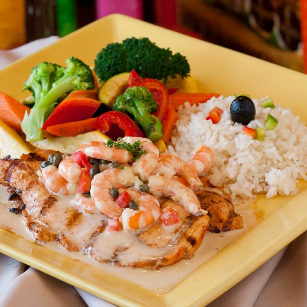 Grilled chicken topped with shrimp in a creamy sauce, served with rice and mixed vegetables.
