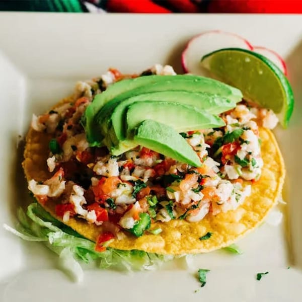 A vibrant Mexican ceviche tostada, topped with fresh avocado slices, lime, and radish.
