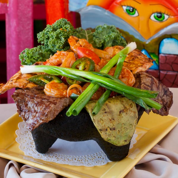 El Coronel's molcajete overflowing with grilled steak, chicken, shrimp, nopales, and green onions.