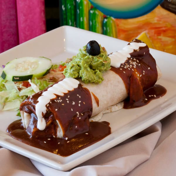 El Coronel's burrito smothered in rich mole sauce, topped with sour cream, guacamole, and a side salad.